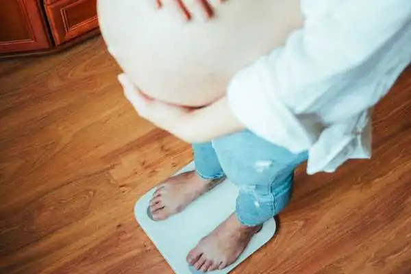 Image of woman weighing herself and experiencing weight gain through pregnancy Telford
